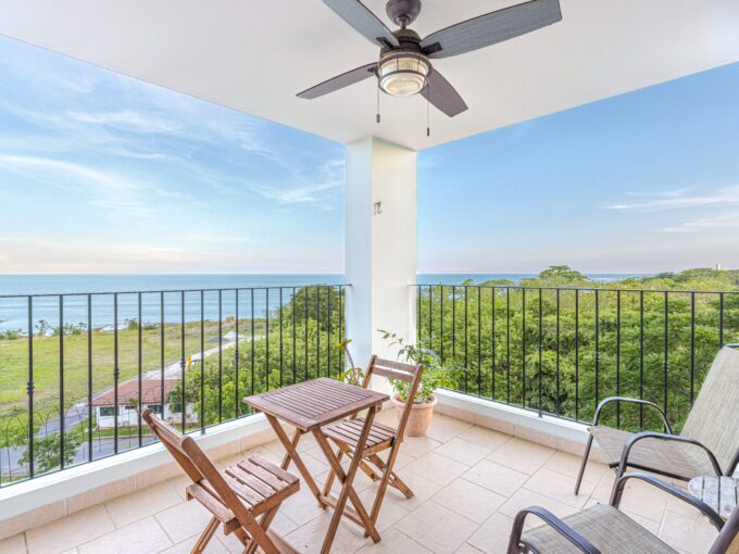 Image of balcony with two chairs, a table and chairs and views of the green spaces and ocean in this condo in Galeones