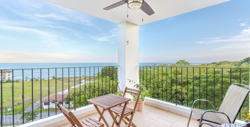 Image of balcony with two chairs, a table and chairs and views of the green spaces and ocean in this condo in Galeones