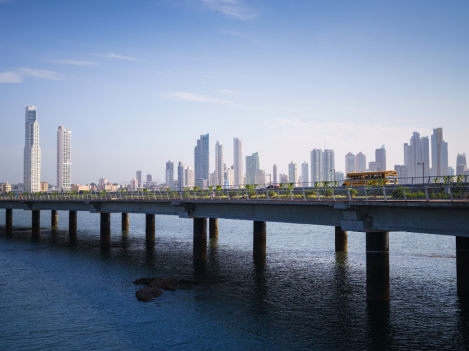 Panama City skyline with modern skyscrapers and bridge over coastal waters featuring a yellow bus, showcasing Santa Ana Panama real estate in Panama City by Panama Equity Real Estate