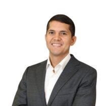 Headshot of Mario, a smiling man with short dark hair wearing a dark grey blazer and open-collar white shirt against a white background.